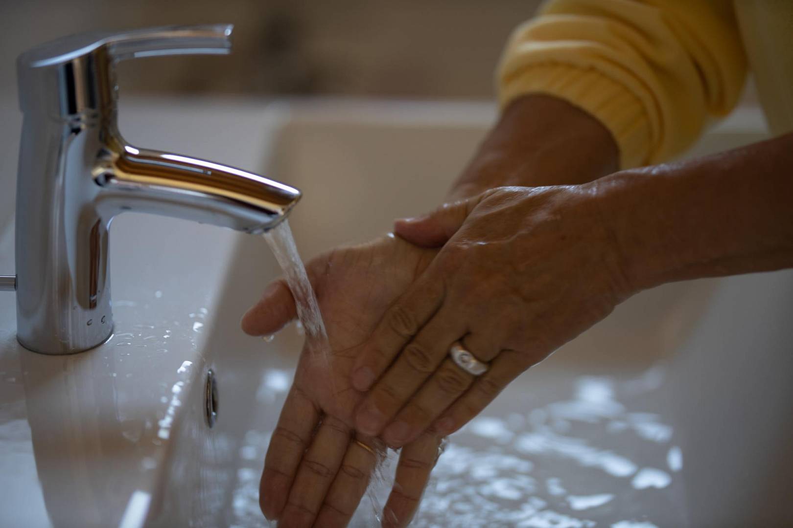 Kobieta myje ręce pod baterią umywalkową w łazience
